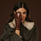 Woman wearing a brown leather glove and a fur-lined coat against a dark background