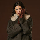 Woman wearing a dark coat with fur collar and brown leather gloves against a brown background