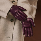 Purple leather gloves worn with a beige coat against a brown background