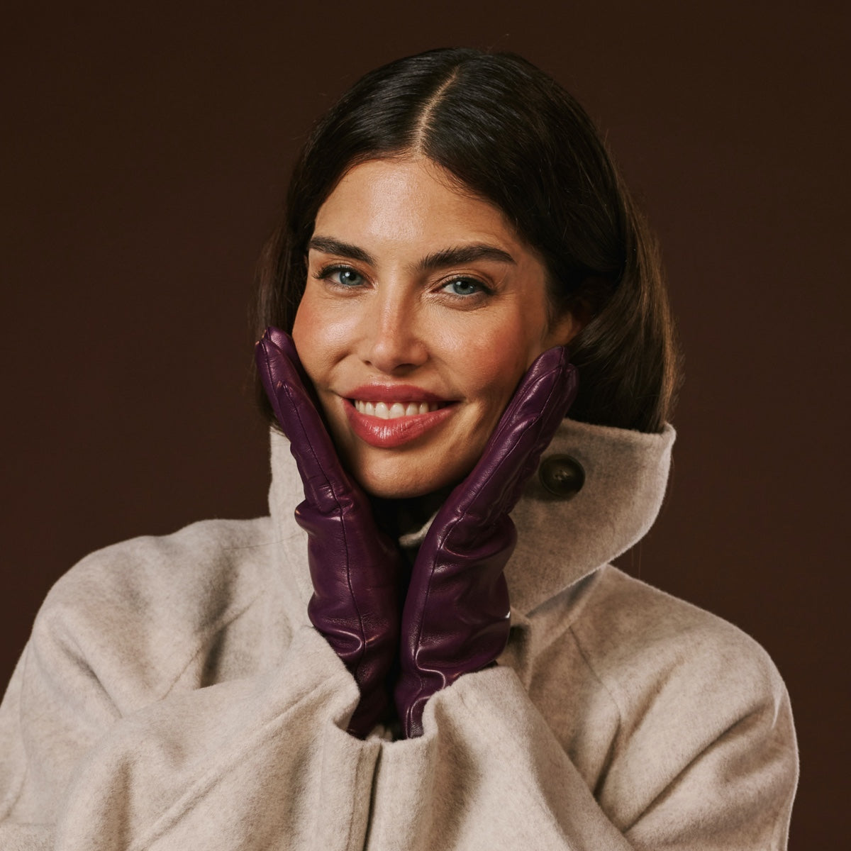 Woman wearing a beige coat and purple leather gloves against a brown background