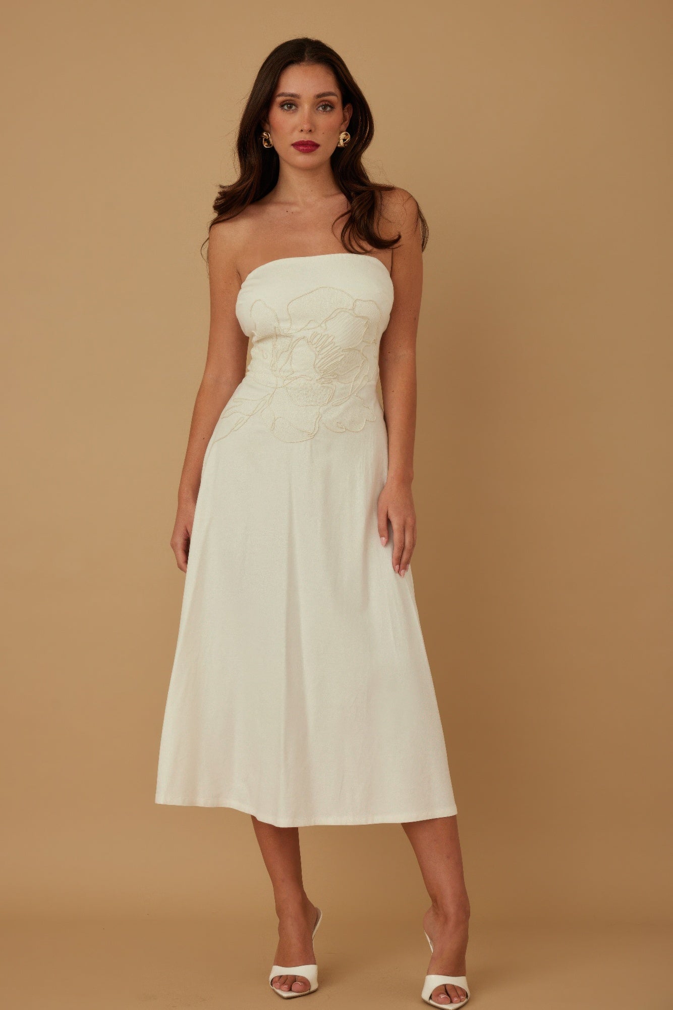 Front view of model wearing ivory strapless embroidered midi dress with white heels
