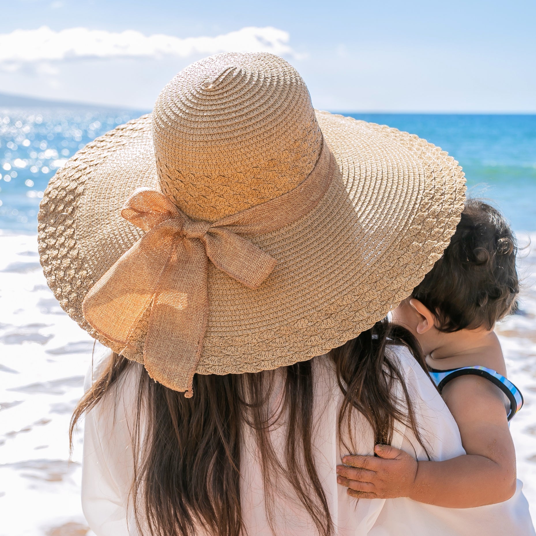 AVAH-woman wearing a large khaki Wide Brim Straw Sun Hat that features a scallop edge design and a burlap bow accent on a beach back view