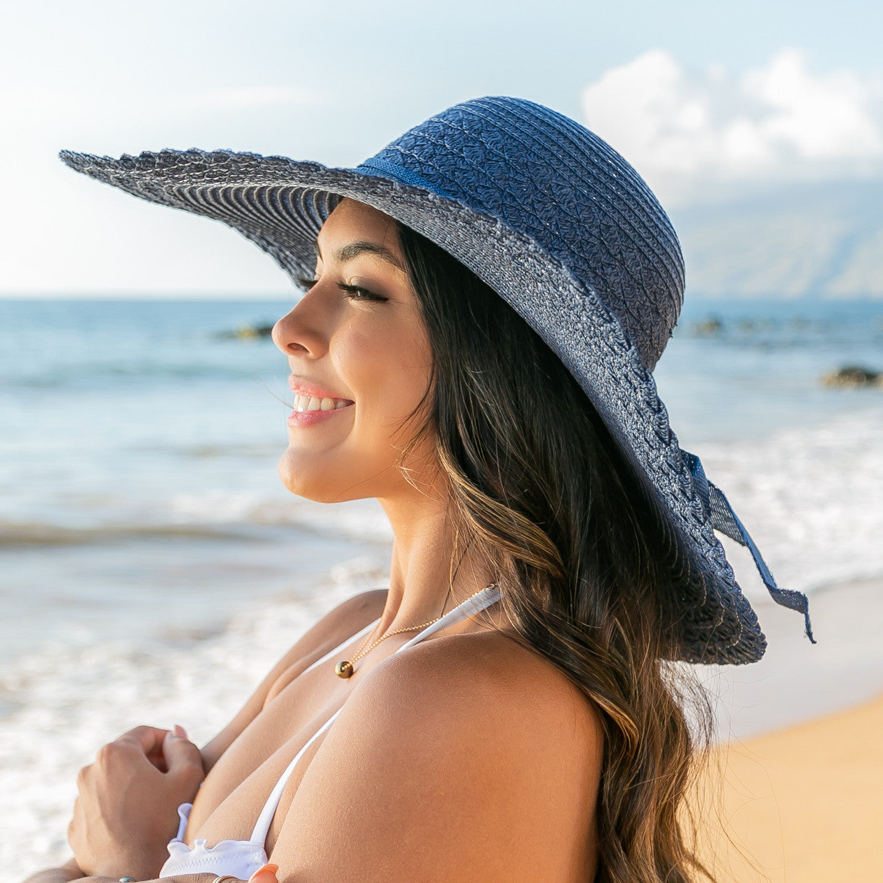 AVAH-Person wearing a large navy-blue Wide Brim Straw Sun Hat that features a scallop edge design and a burlap bow accent on a beach side view