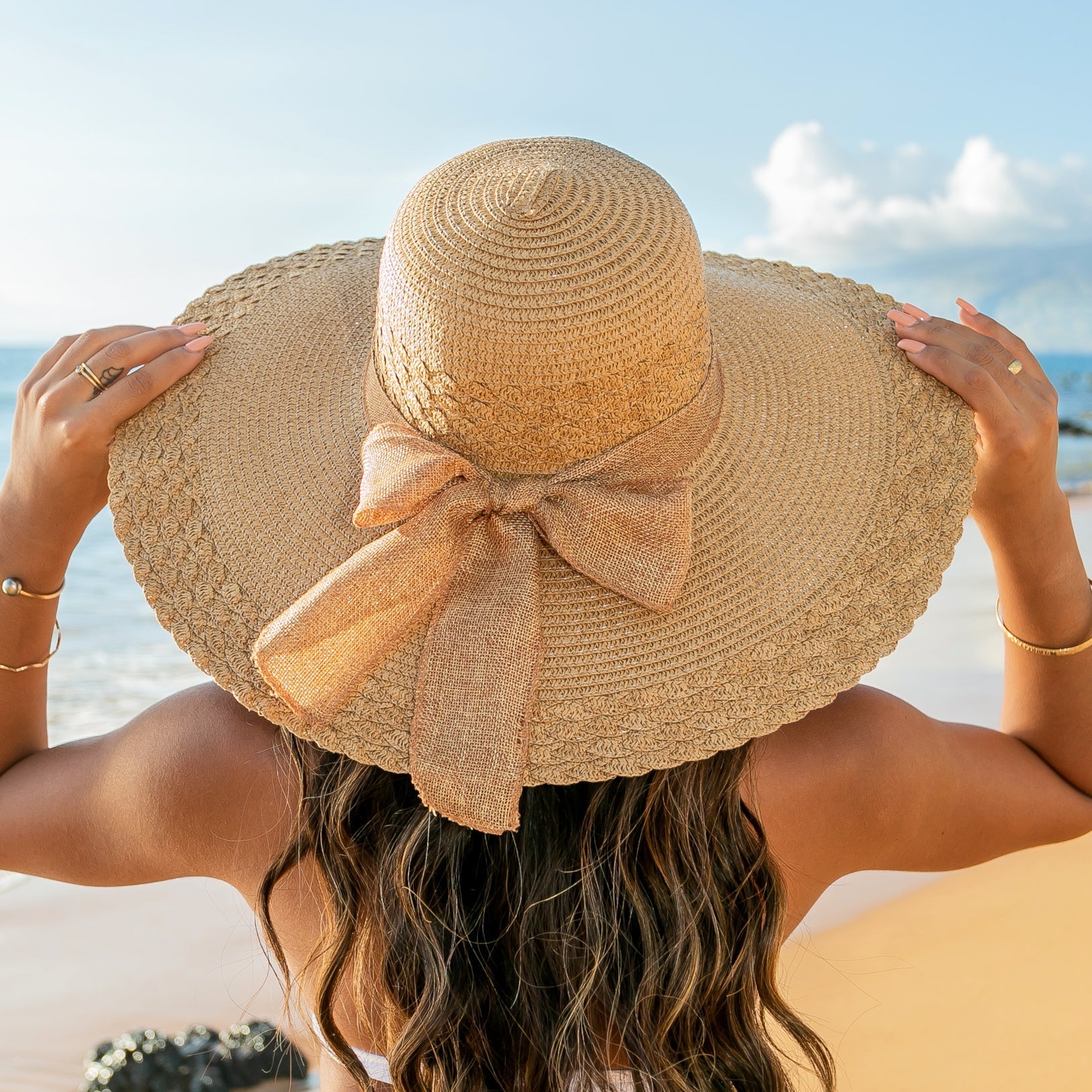 AVAH-woman wearing a large khaki Wide Brim Straw Sun Hat that features a scallop edge design and a burlap bow accent on a beach back view