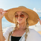 AVAH-woman wearing a large Wide Brim Straw Sun Hat that features a scallop edge design and a burlap bow accent on a beach front view