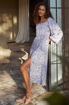 Woman in a lavender floral midi dress with puff sleeves and slit standing on stone steps outdoors