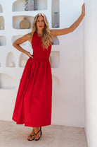 Woman in a red cotton sleeveless midi dress posing in a room with decorative wall shelves.