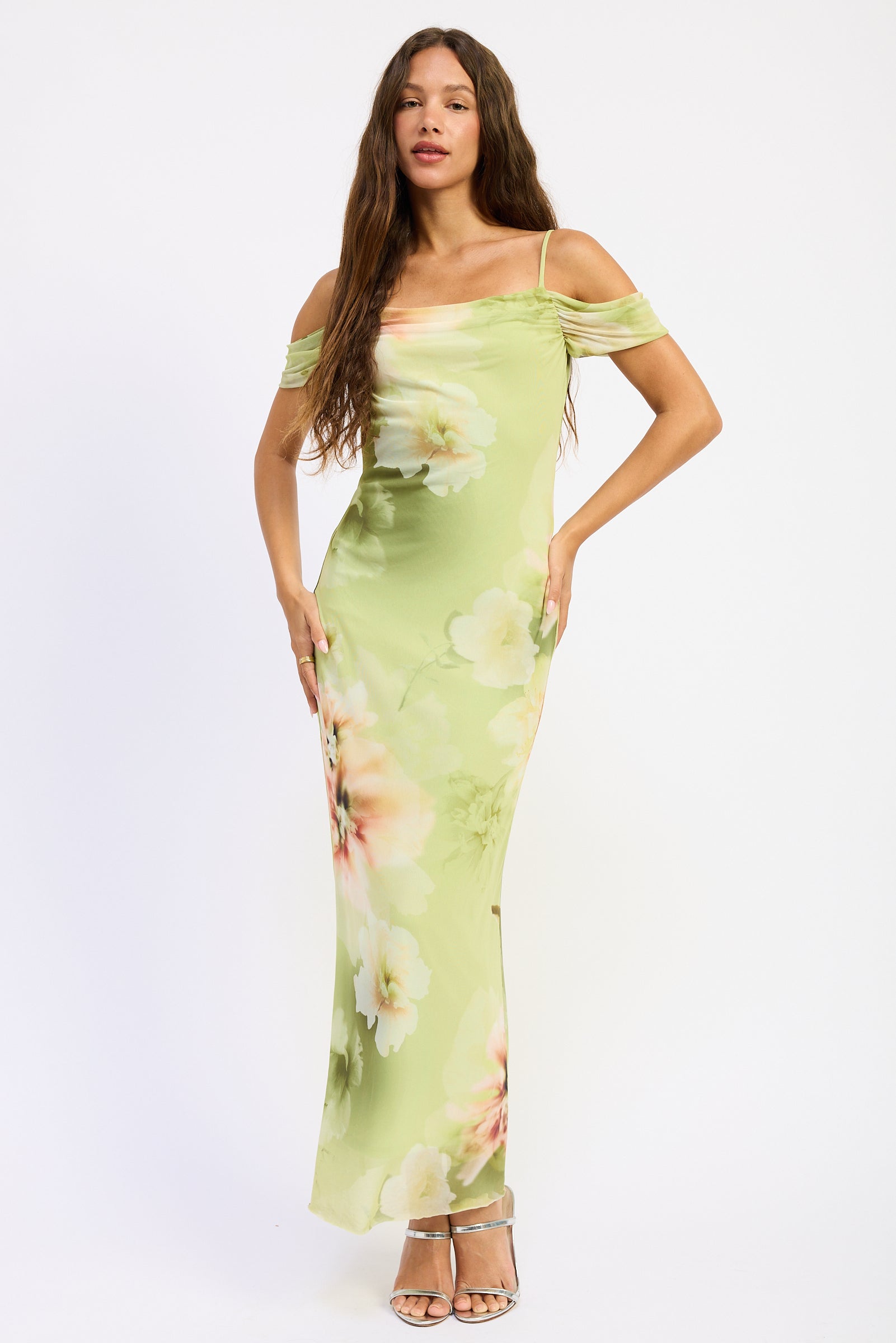 Woman wearing a soft green floral off shoulder maxi dress with ruched sleeves and fitted silhouette
