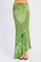Woman wearing a green orchid print floral maxi skirt and matching open back cami top with slim straps sleeveless top with a white background front view