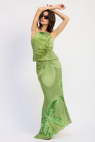 Woman wearing a green orchid print floral maxi skirt and matching open back cami top with slim straps sleeveless top with a white background front view