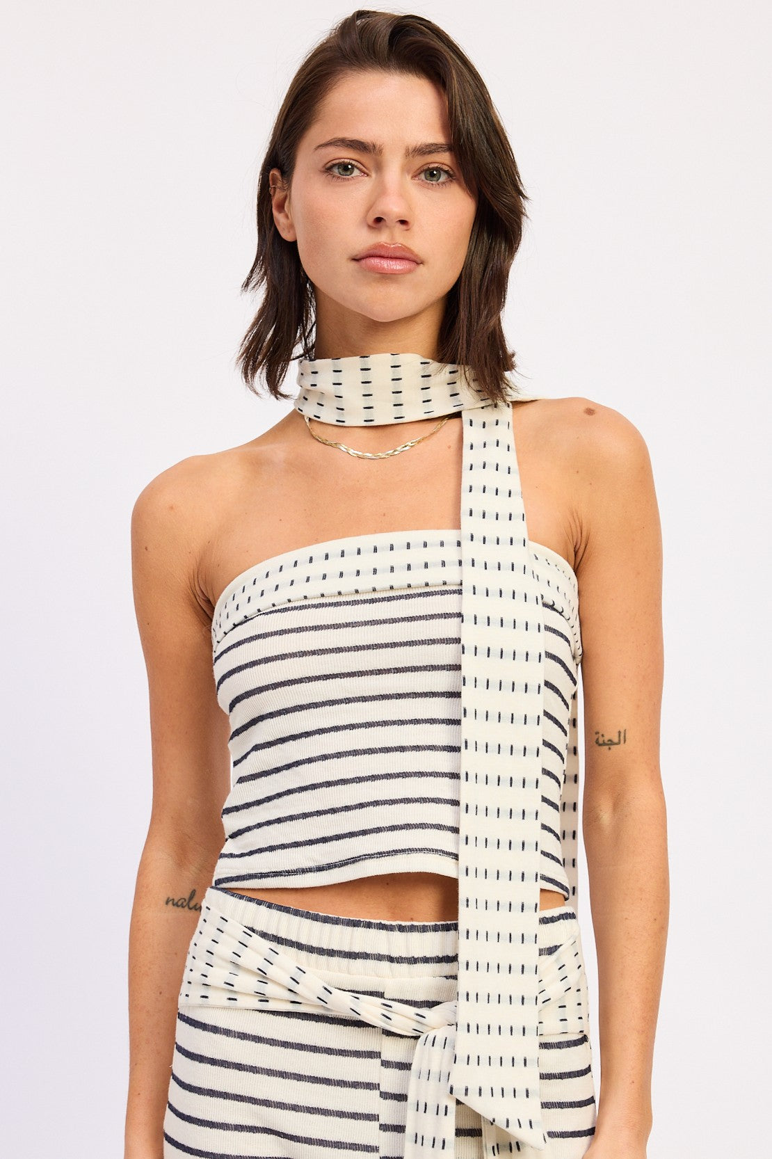 Woman wearing an ivory striped bandeau top with a scarf on a white background