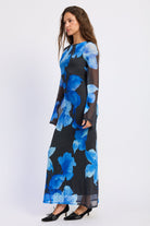 Side view of Blue Reverie Floral Long Sleeve Maxi Dress featuring vivid blue flowers, boat neckline and long sheer sleeves.