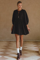 Woman wearing a black dress with long sleeves in a room with a checkered floor.