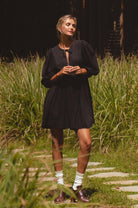 Woman in a black dress standing on a path surrounded by tall grass.