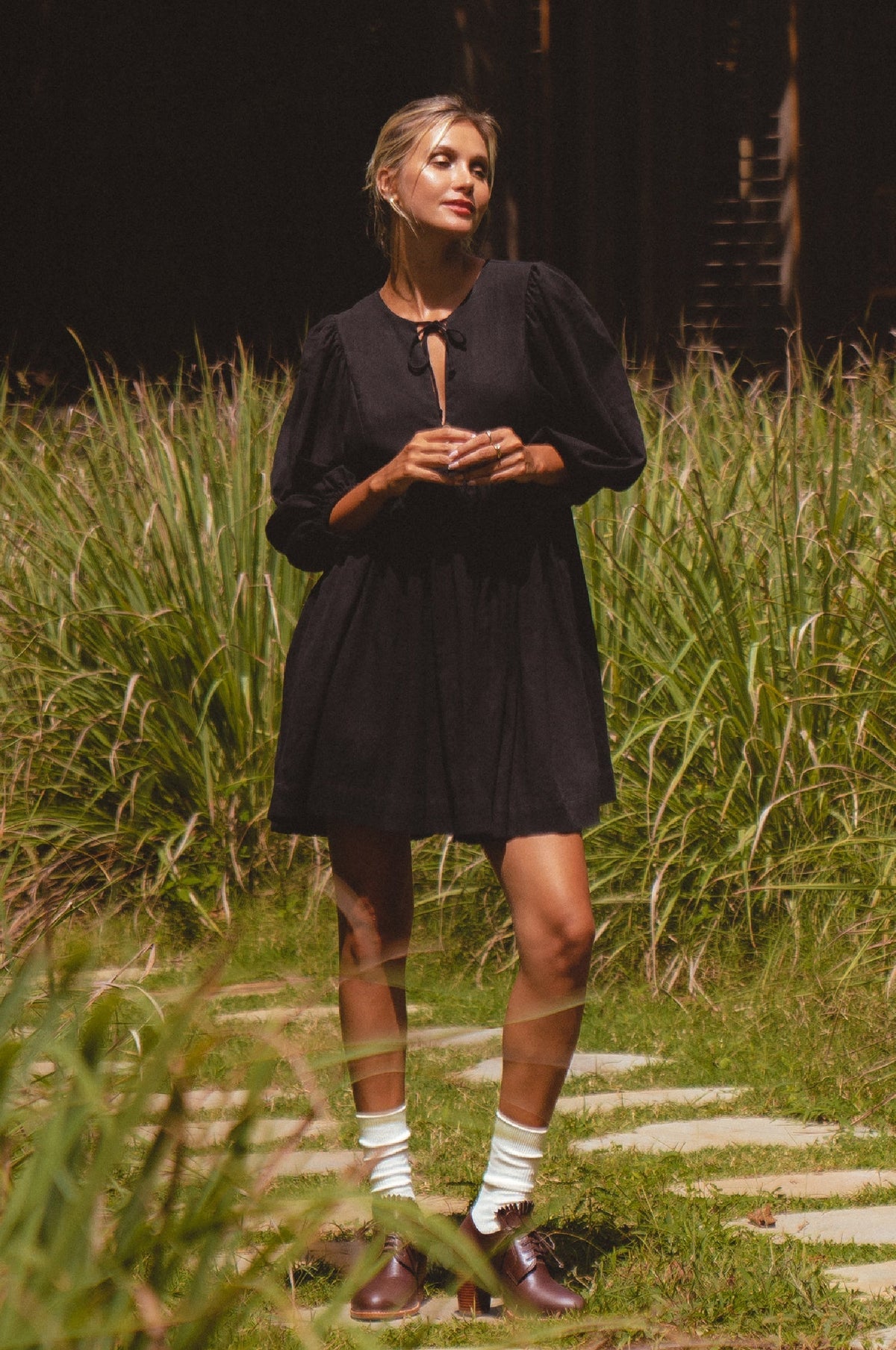 Woman in a black dress standing on a path surrounded by tall grass.