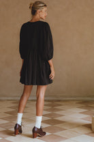 Woman wearing a black dress standing in a room with a checkered floor.