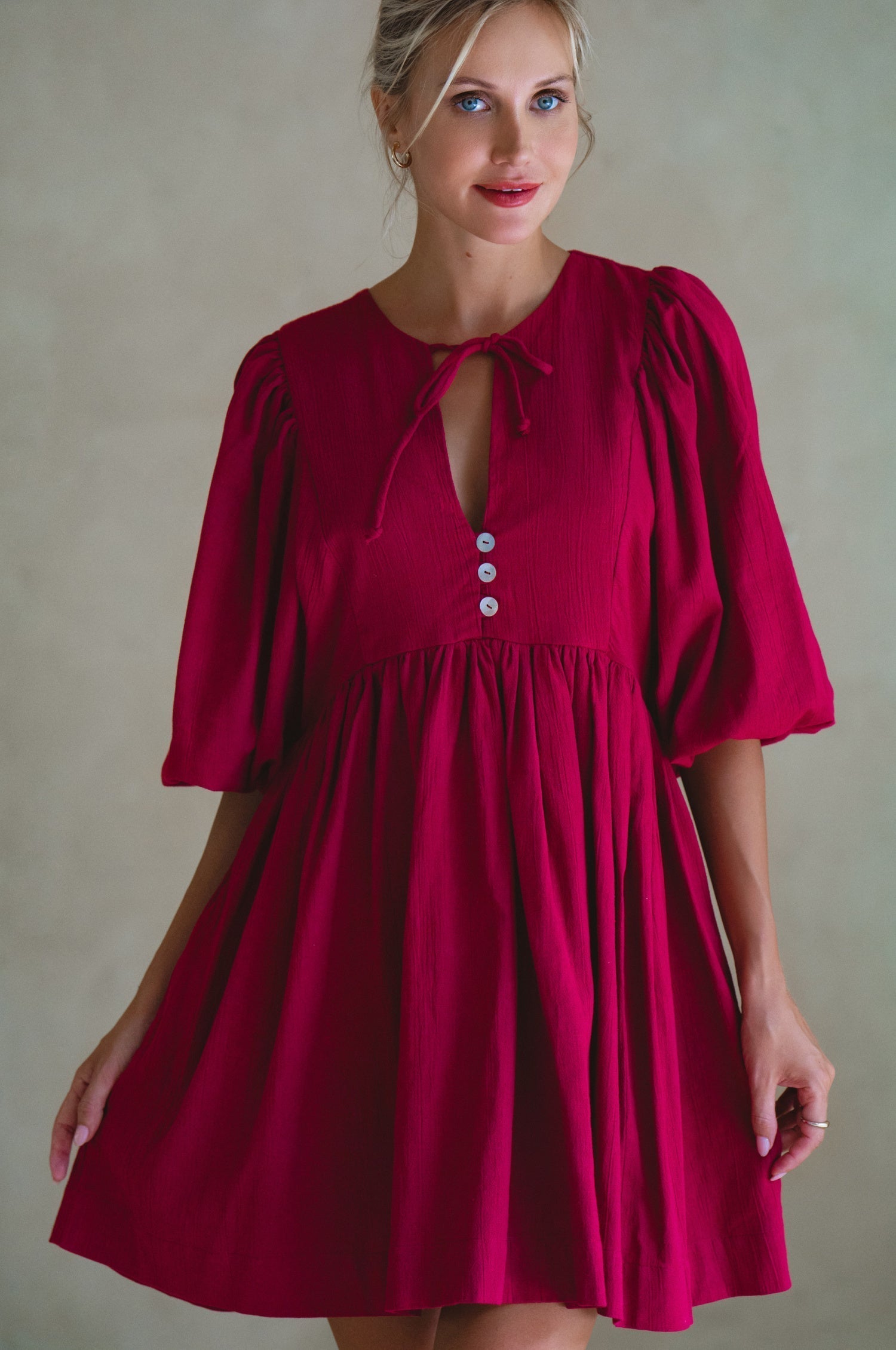 Woman wearing wine colored linen mini dress or lightweight crinkle linen in a long-sleeve babydoll silhouette against a neutral background, front view