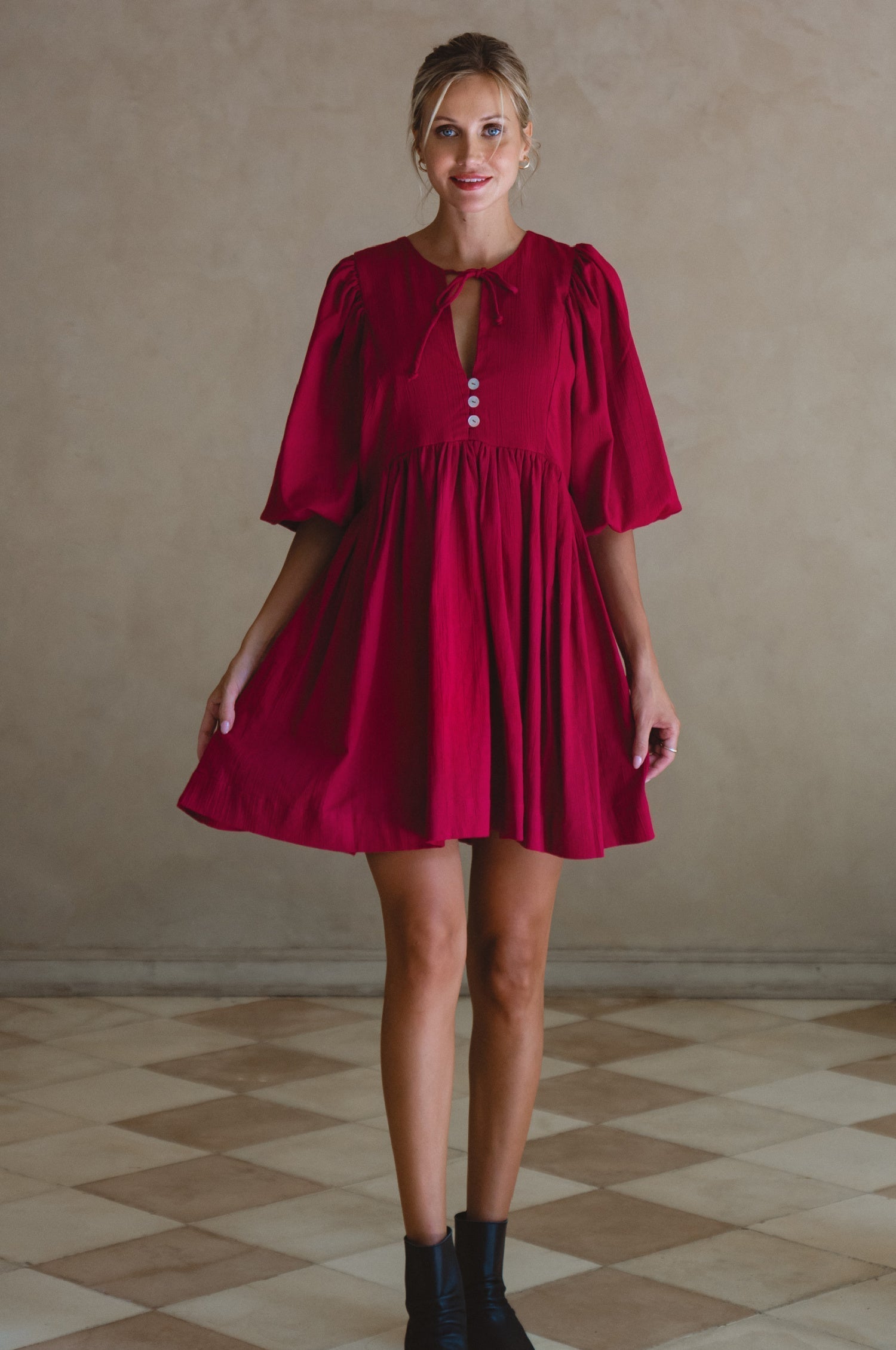 Woman wearing wine colored linen mini dress or lightweight crinkle linen in a long-sleeve babydoll silhouette against a neutral background, front view