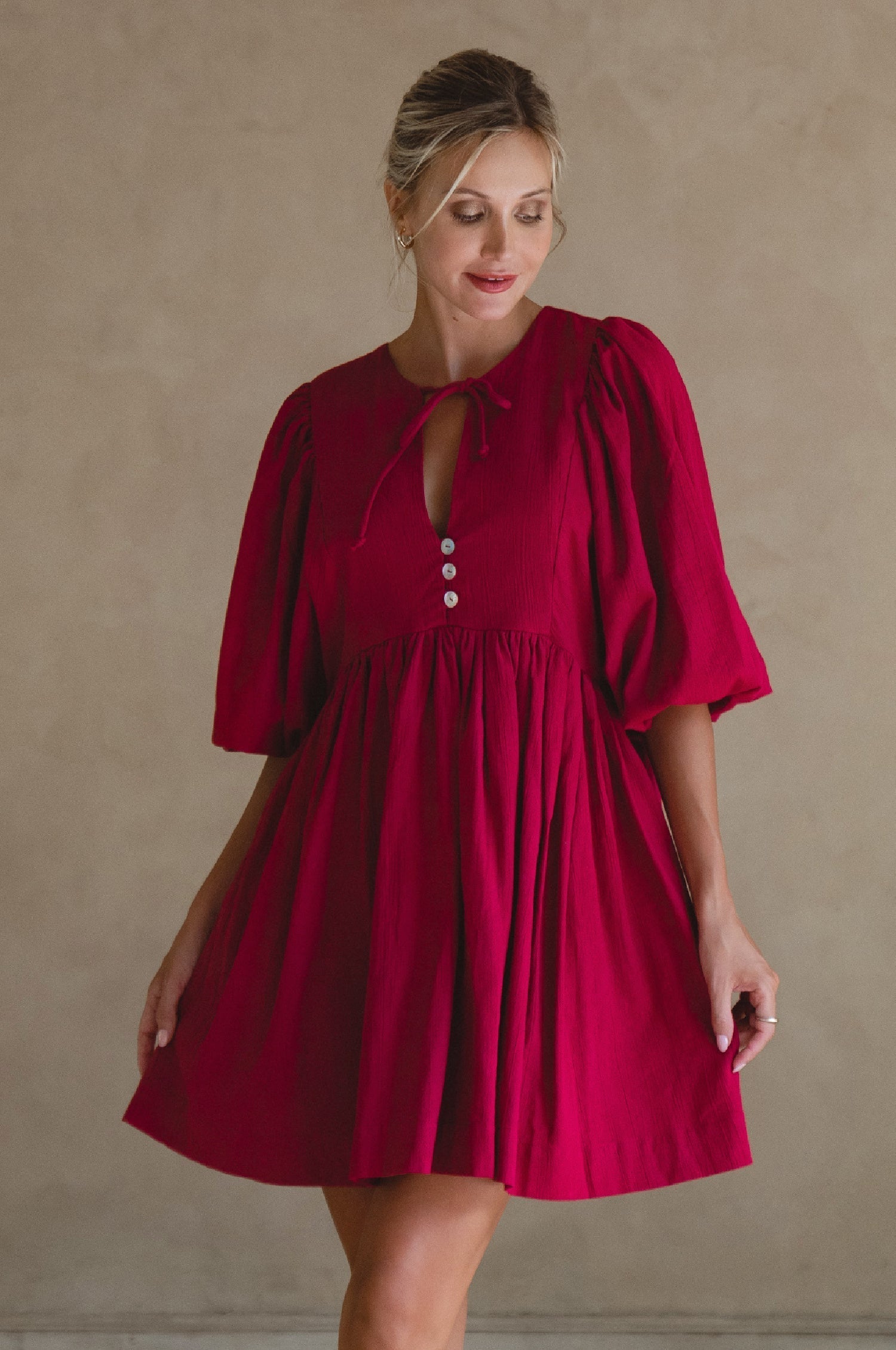 Woman wearing wine colored linen mini dress or lightweight crinkle linen in a long-sleeve babydoll silhouette against a neutral background, front view