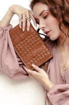 Woman holding a brown leather woven clutch bag against a plain background
