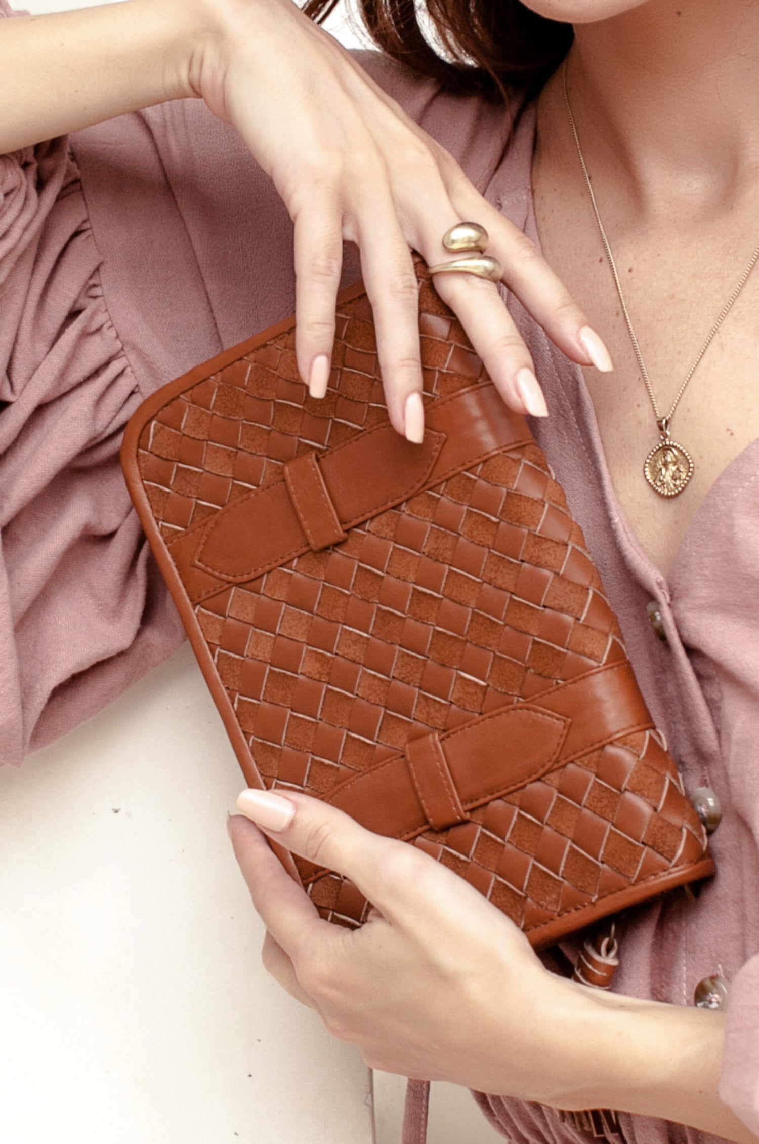 Brown leather woven clutch held by a person wearing a pink top.
