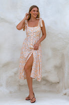 Woman wearing a cream floral square neckline and button-down fit-and-flare midi dress with adjustable tie-up straps and a smocked back against a neutral background, front view