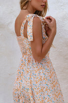 Woman wearing a floral square neckline and button-down fit-and-flare midi dress with adjustable tie-up straps and a smocked back against a neutral background, side view