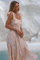 Woman wearing a floral square neckline and button-down fit-and-flare midi dress with adjustable tie-up straps and a smocked back against a neutral background, 3/4view