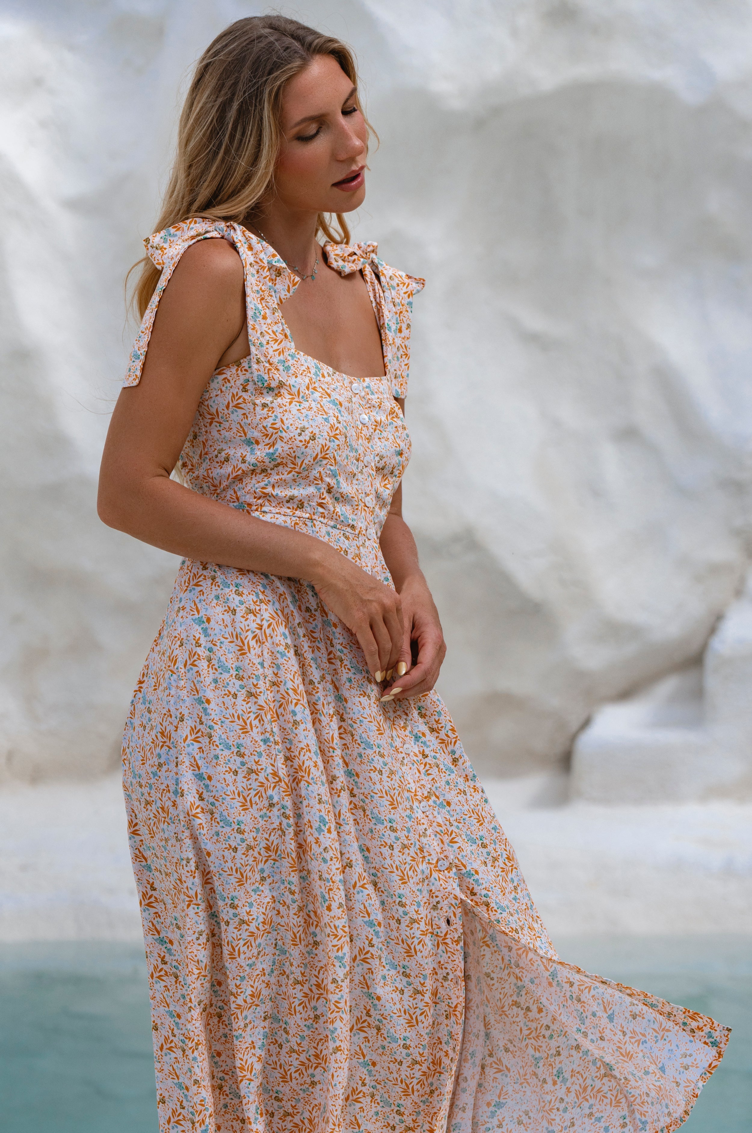 Woman wearing a floral square neckline and button-down fit-and-flare midi dress with adjustable tie-up straps and a smocked back against a neutral background, 3/4view
