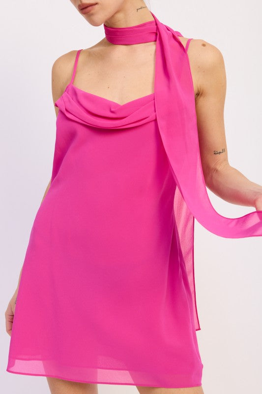 Woman wearing a bright pink mini dress with cowl neckline and scarf on a white background front view