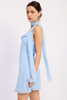 Woman wearing a light blue mini dress with cowl neckline and scarf on a white background side view