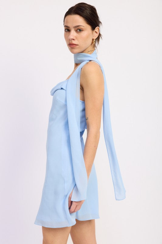 Woman wearing a light blue mini dress with cowl neckline and scarf on a white background side view