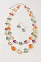 A gold-tone jewelry set featuring a multi-strand necklace and matching drop earrings, embellished with round, faceted gemstones in vibrant shades of orange, teal, green, purple, and clear, displayed on a light off-white background.