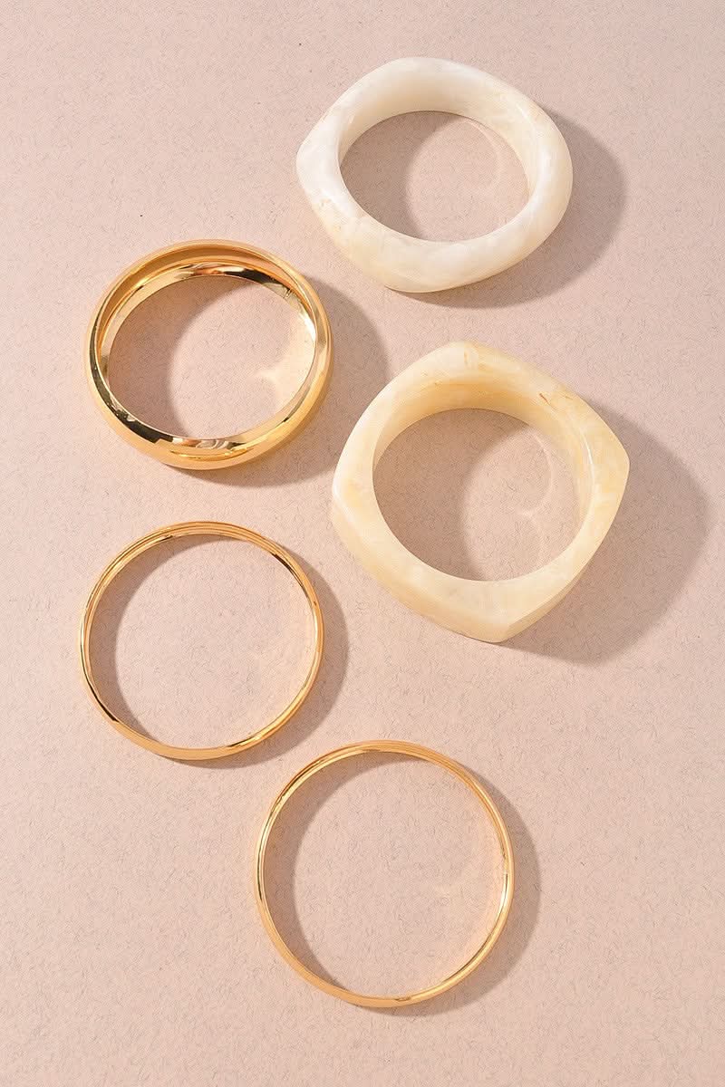 Five bangle bracelets arranged on a warm beige background: three slim gold-tone bands and two chunkier marbled beige bands with organic shapes.