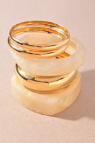 Set of gold bangles and marbled beige resin bangles stacked on a beige background