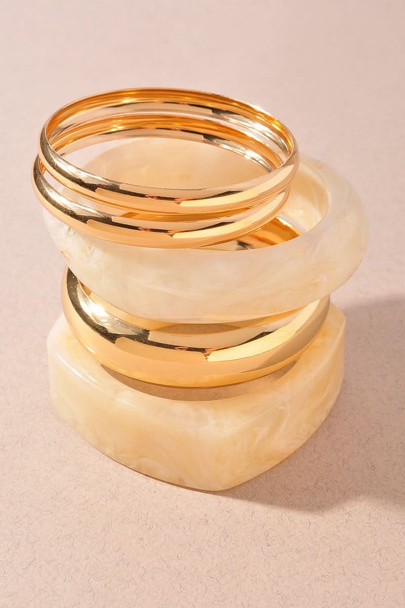 Set of gold bangles and marbled beige resin bangles stacked on a beige background