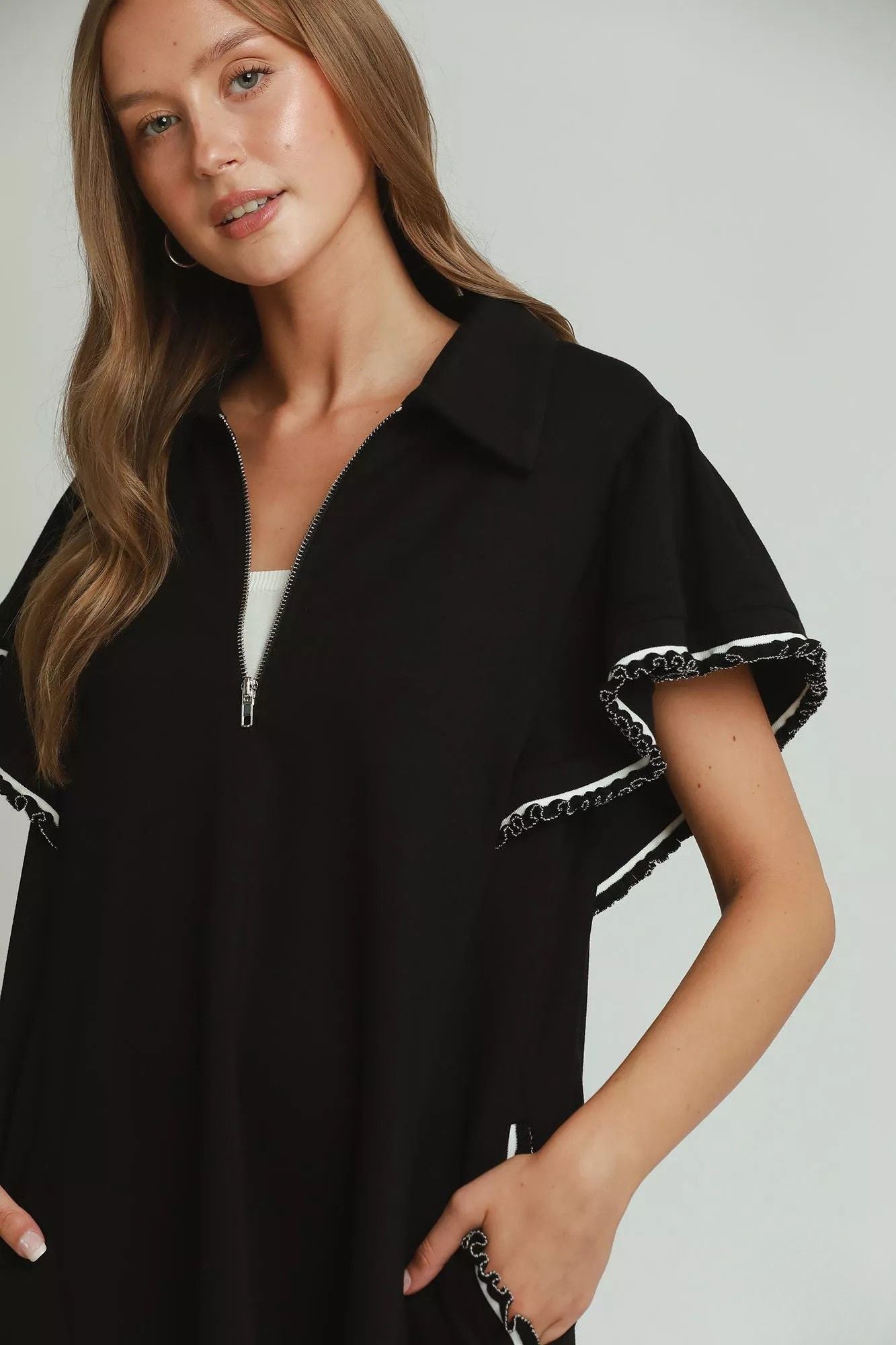 Close detail of black half zip neckline and contrast looped trim on flutter sleeve, AVAH