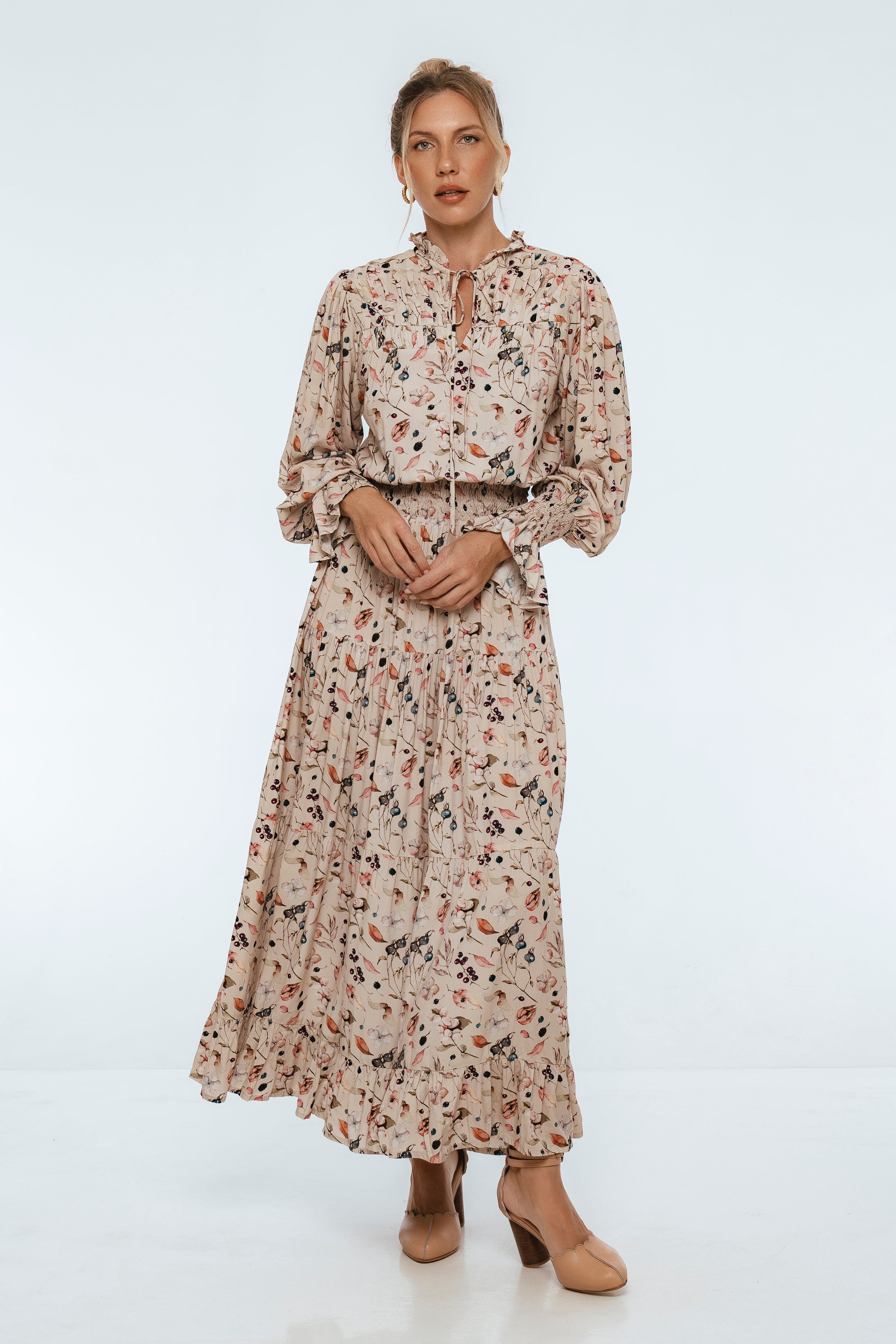 woman wearing a cream floral maxi dress standing against a gray background