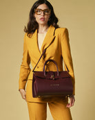 Woman in a yellow suit holding a maroon handbag against a beige background