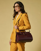 Woman in a mustard yellow suit holding a burgundy handbag against a beige background
