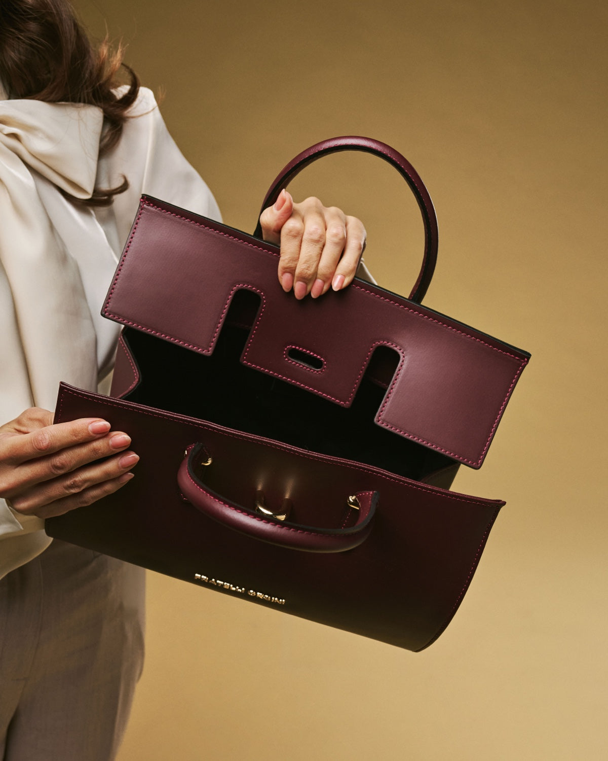 Person holding a burgundy handbag against a beige background
