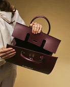 Person holding a burgundy handbag against a beige background