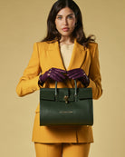 Woman in mustard suit holding a green handbag against a beige background