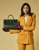 Woman in mustard yellow suit holding a green handbag against a beige background