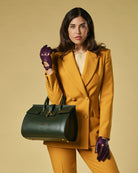 Woman in mustard yellow suit holding a green leather  handbag against a beige background