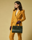 Woman in mustard yellow suit holding a green leather handbag against a beige background