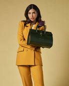 Woman in a mustard yellow suit holding a green leather handbag against a beige background