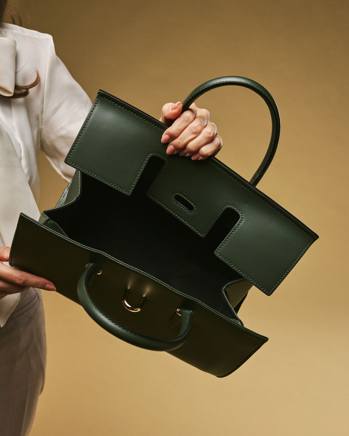Green handbag held by a person against a beige background