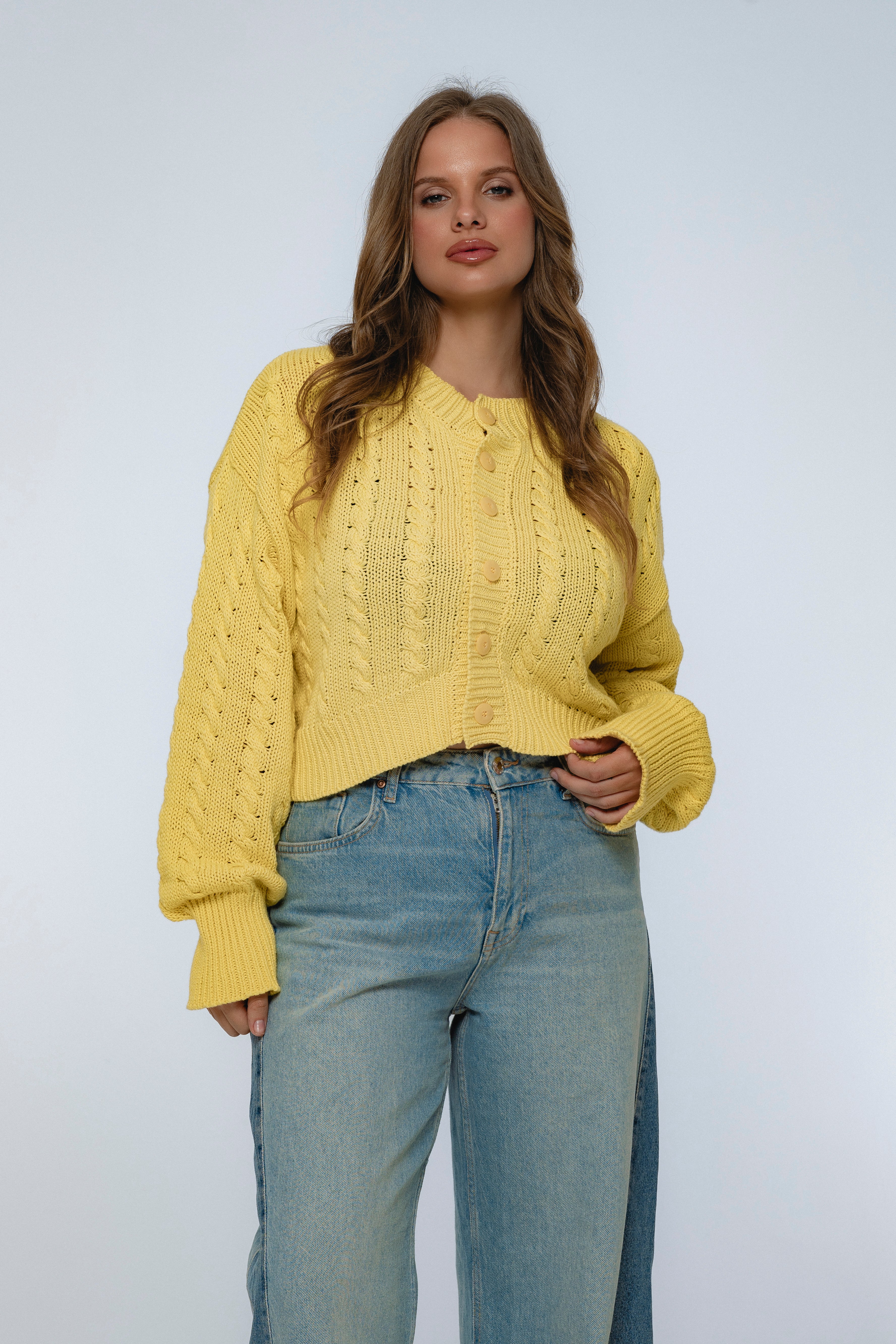 Woman wearing a yellow knitted sweater and blue jeans against a light gray background