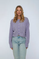 Woman wearing a light purple cardigan and light blue jeans against a white background